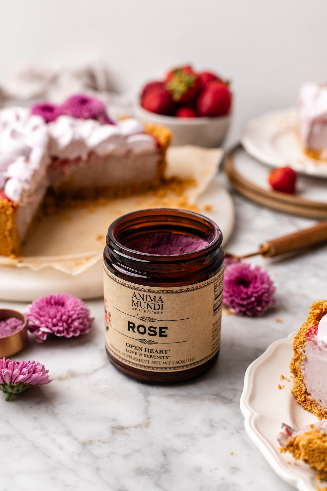 Jar of Anima Mundi Rose cream on a marble surface with desserts and flowers in the background