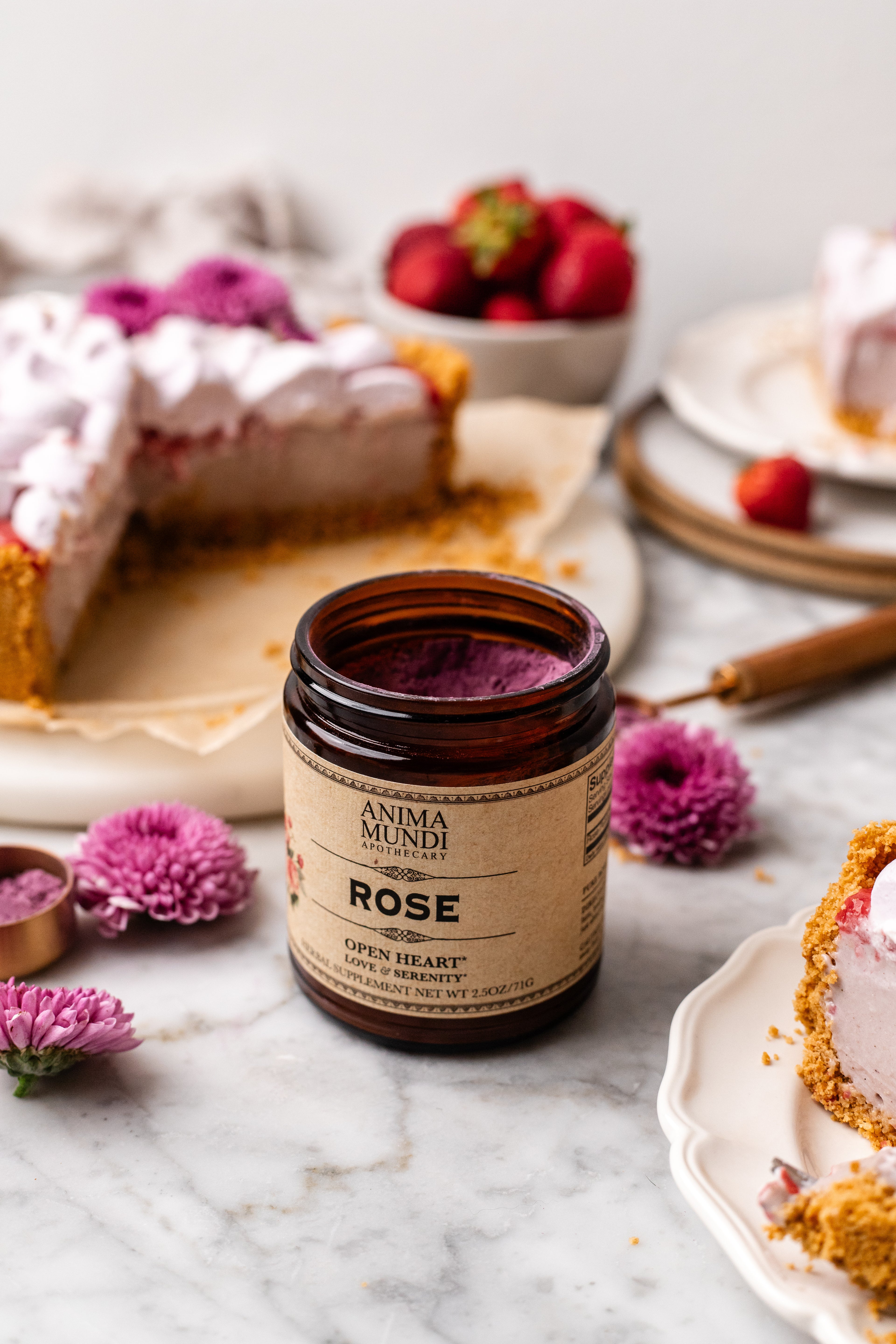 Jar of Anima Mundi Rose cream on a marble surface with desserts and flowers in the background