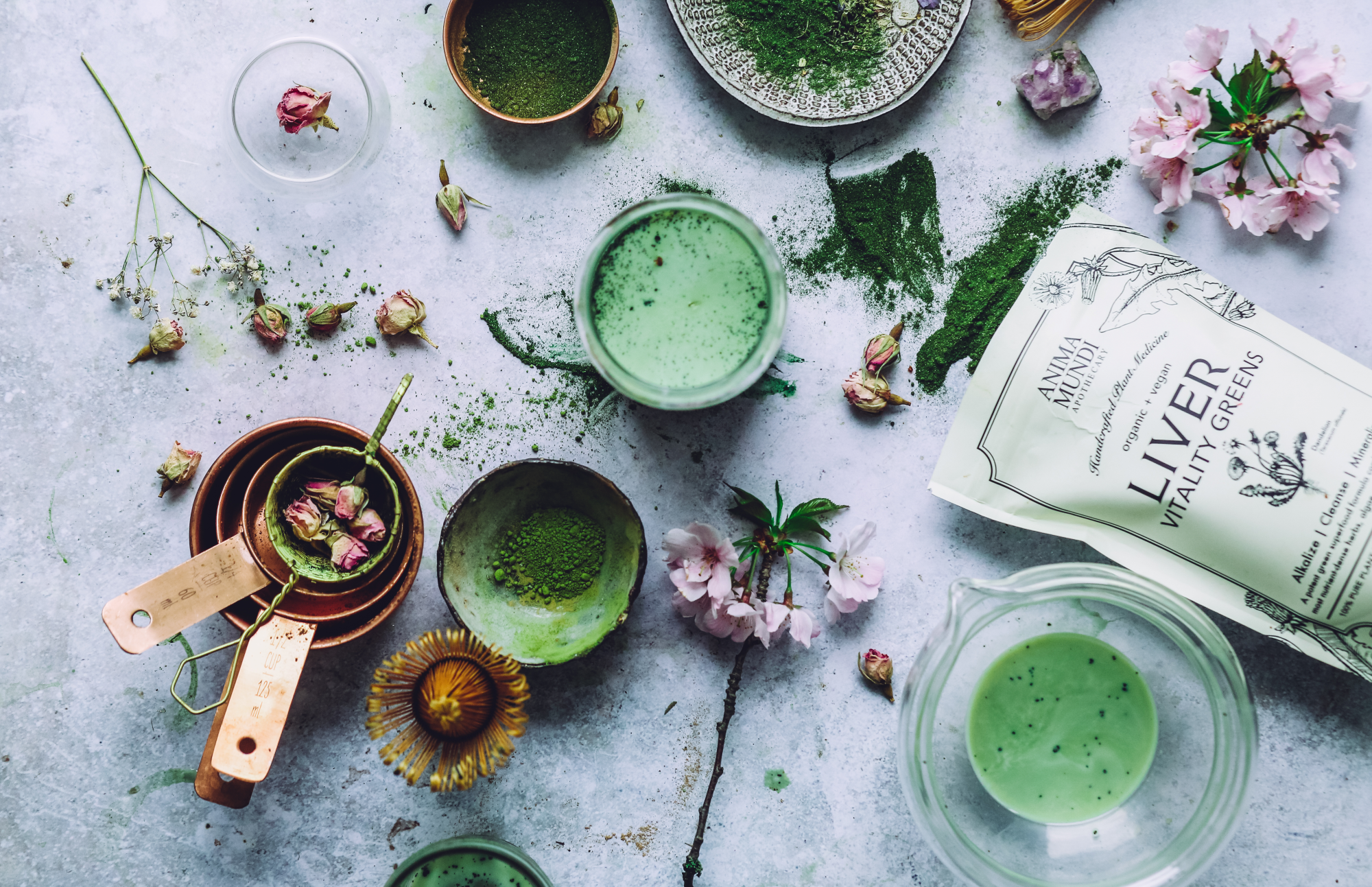 Green smoothie in a bowl with ingredients from anima mundi herbals and packaging on a light surface
